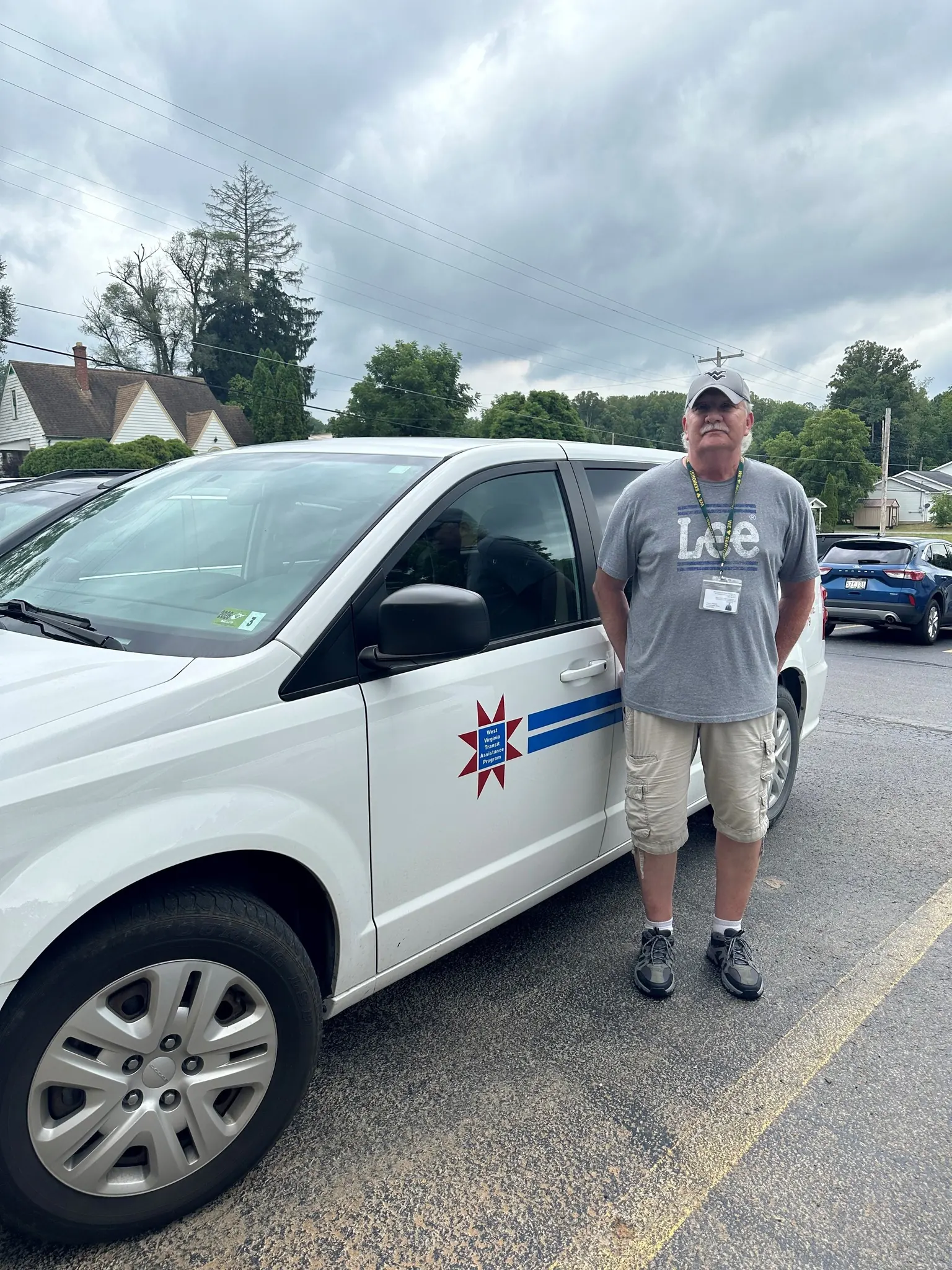 A male driver in casual clothing, wearing a Marion Senior Centers name badge, stands beside the Marion Senior Centers Transportation Van.