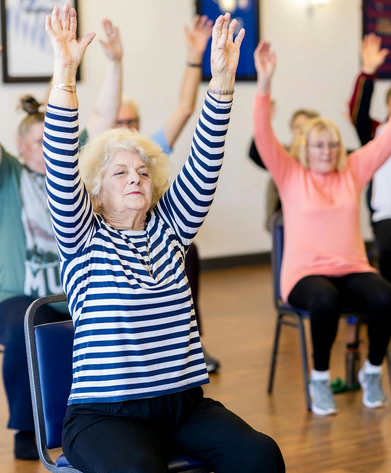 A group of seniors participate in group exercise from a seated position