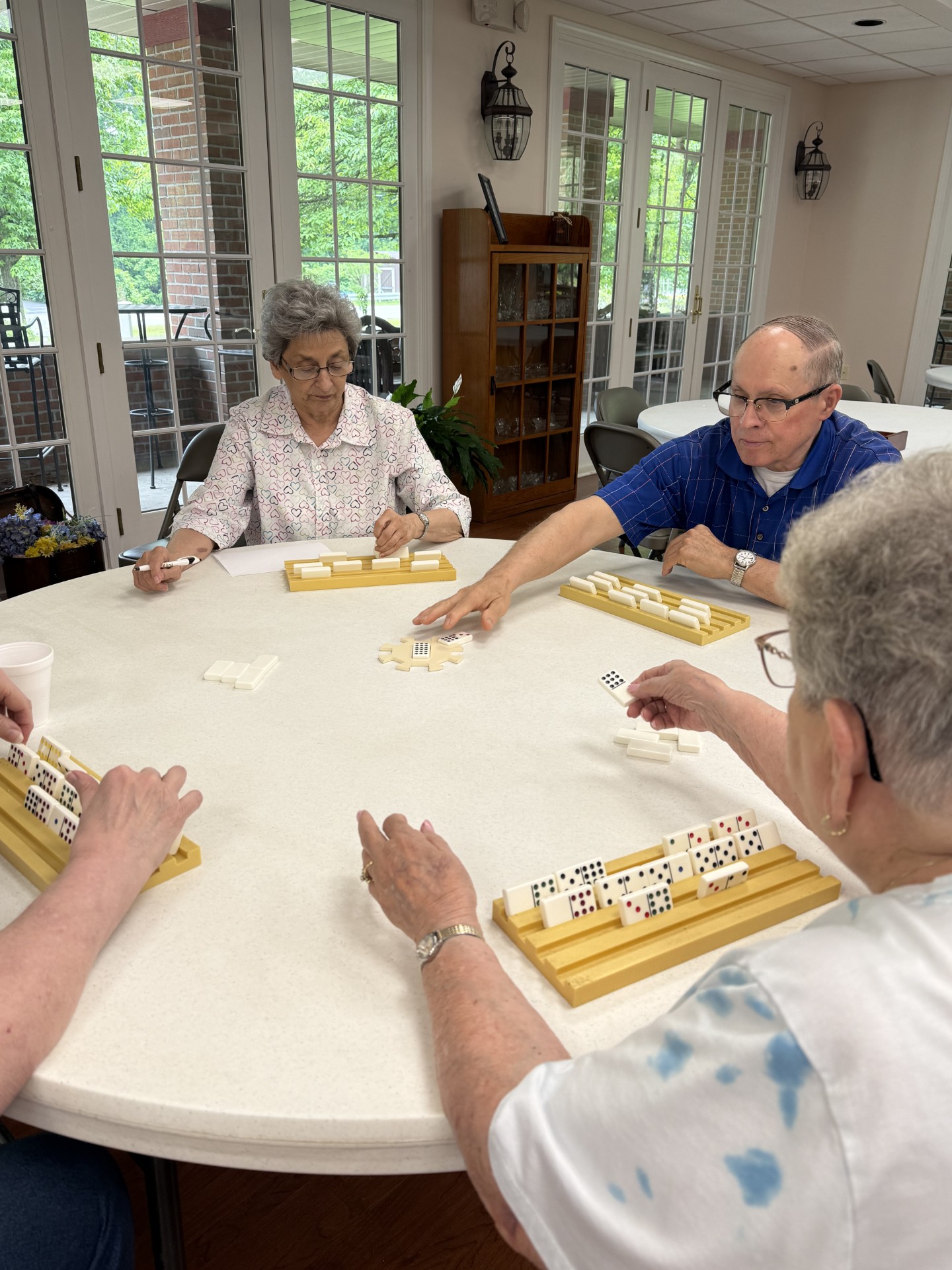 seniors sitting around a white round table playing a domino game called Chicken Foot