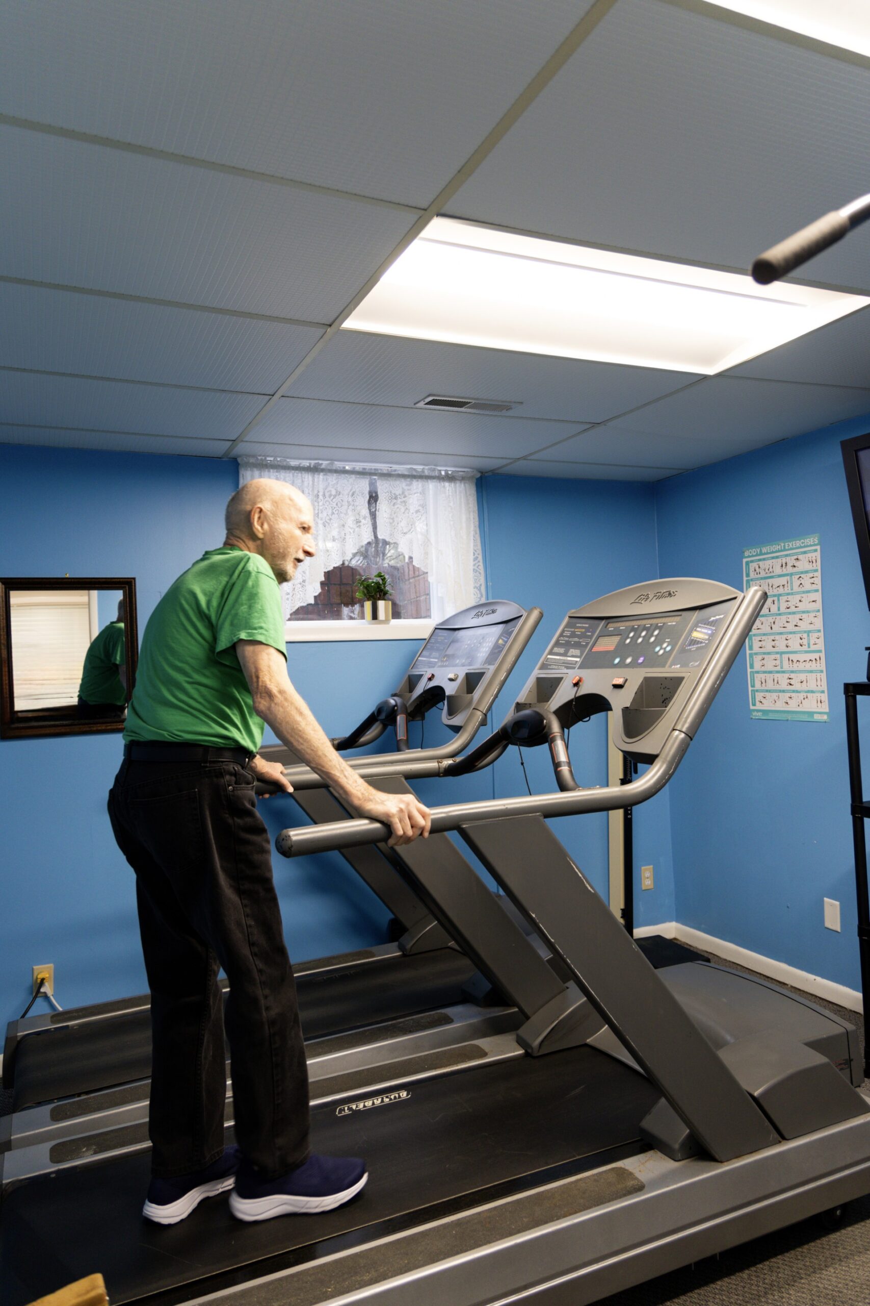 older gentleman in black pants and green tee walking on a treadmill
