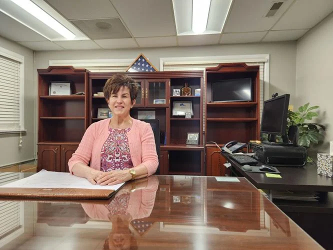 woman with dark hair dressed in pink sitting behind a large desk