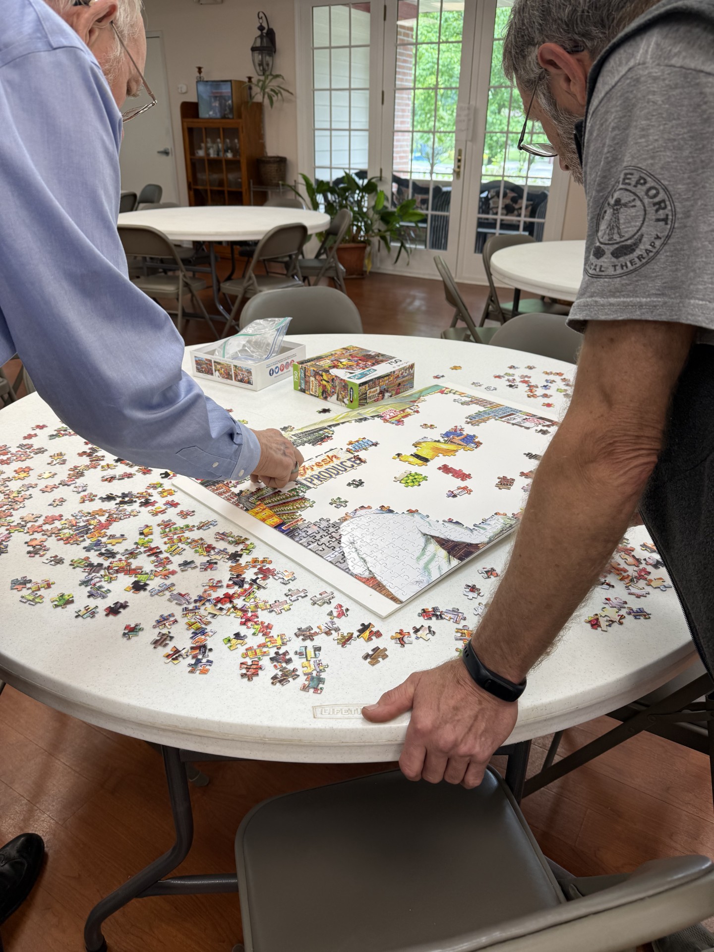 two men working at a large white round table putting a puzzle together